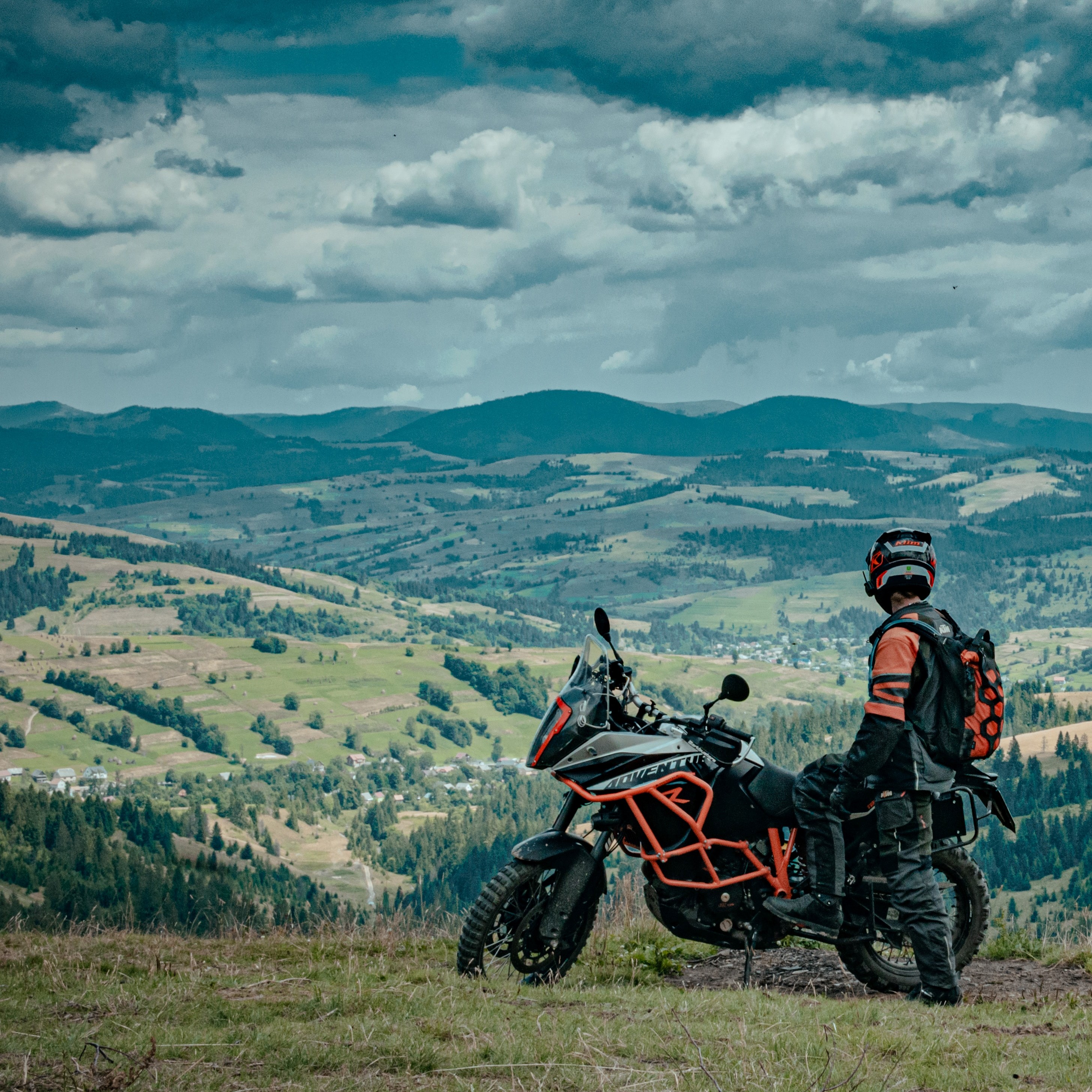 un homme avec sa moto de dos qui regarde un paysage de campagne